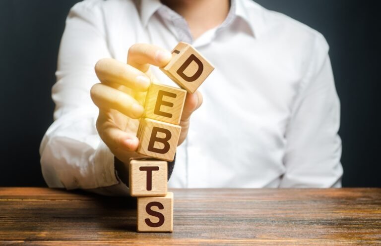 A man breaks a tower of blocks with the word Debts. Reduction or restructuring of debt. Bankruptcy. Refusal to pay. Heavily indebted citizens low financial literacy. Get out of Debt